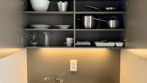 Una cocina moderna con un lavamanos de acero inoxidable, dos hornallas y una variedad de utensilios de cocina, incluyendo ollas, sartenes y cristalería.