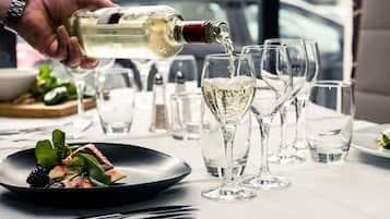 A dining table with a plate of food, glasses, and a bottle of white wine being poured.