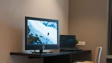 A modern office desk with a large monitor displaying a snowy mountain scene, a laptop, and a small plant.