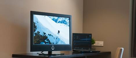Un escritorio moderno de oficina con un monitor grande que muestra una escena de montaña nevada, una computadora portátil y una pequeña planta.