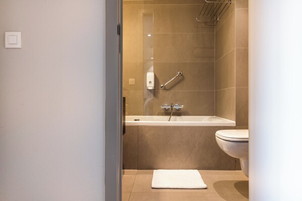 A modern bathroom with a bathtub, toilet, and a glass shower enclosure. - Aparthotel Castelnou (Ghent)