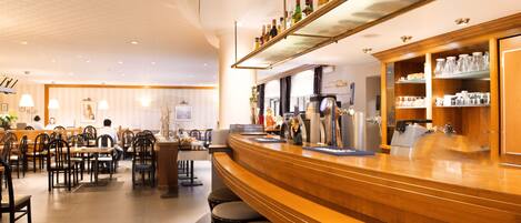 Zona de bar con taburetes, barra y estanterías con botellas y copas.