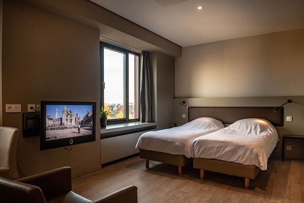 Habitación de hotel moderna con un ventanal grande, televisión de pantalla plana, dos camas, un escritorio y una silla.