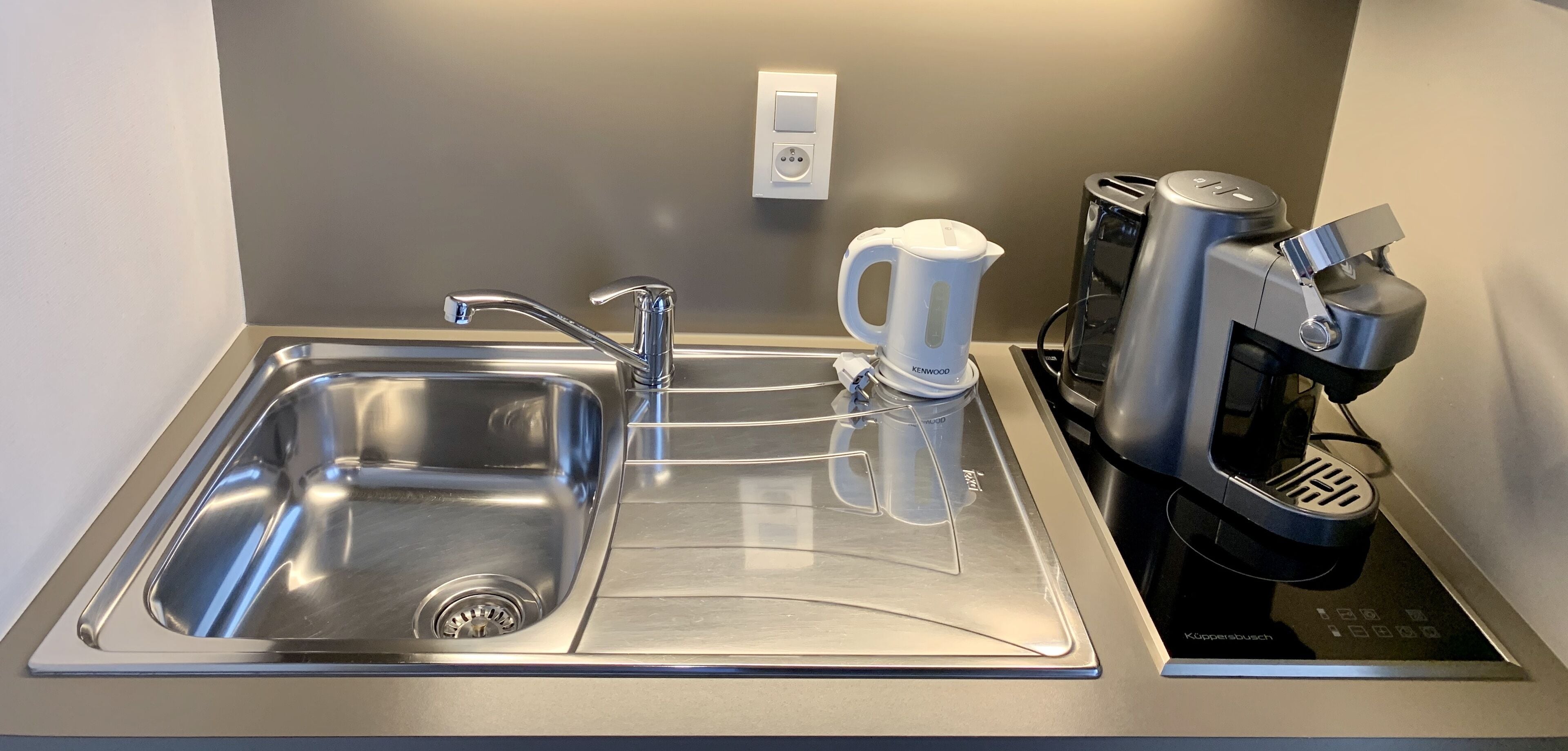 A modern kitchen with a stainless steel sink, a kettle, and a coffee maker.