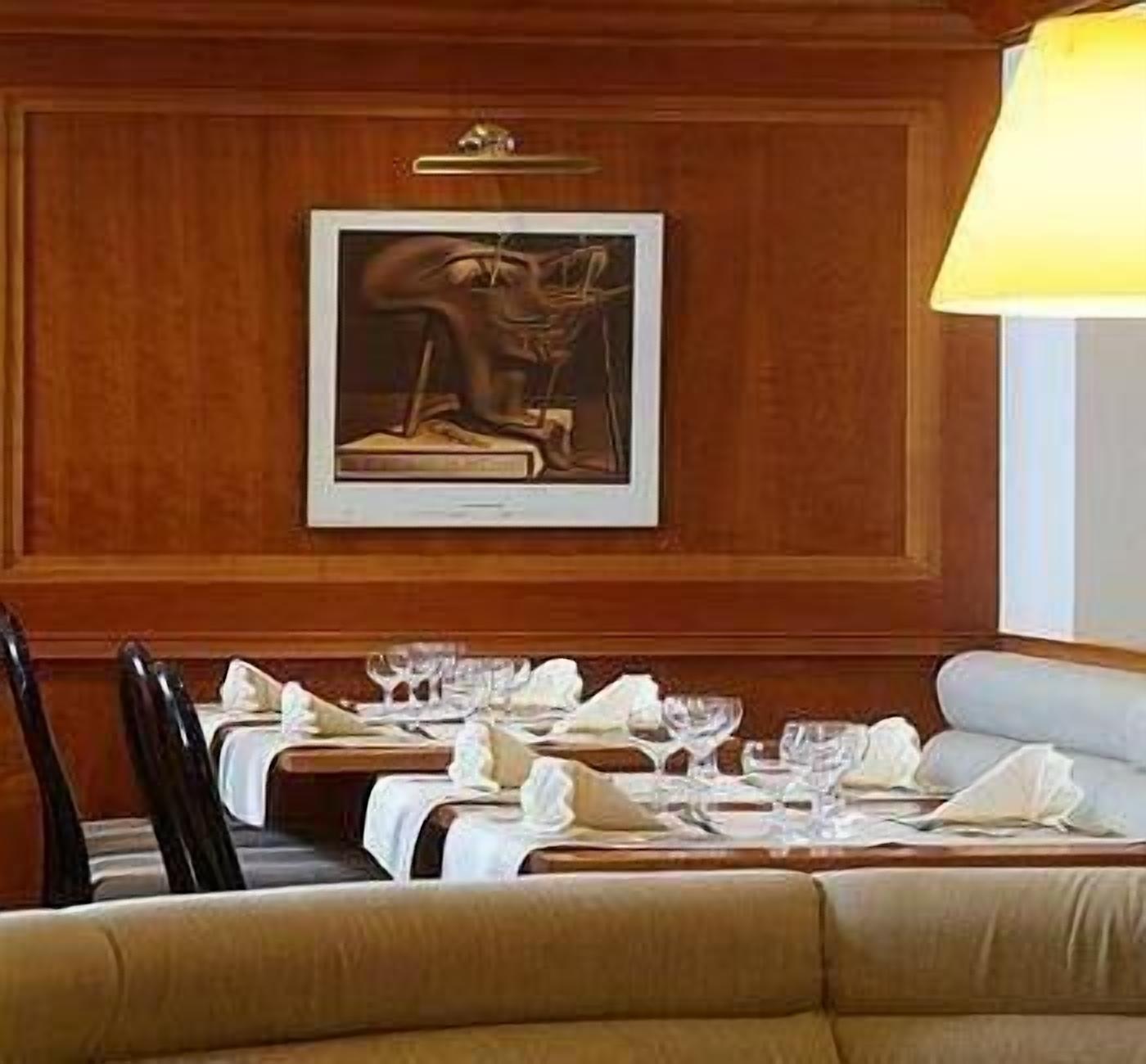 A dining area with wooden paneling, a framed painting above the tables, and a lamp on the right.