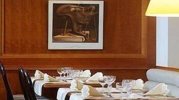 A dining area with wooden paneling, a framed painting above the tables, and a lamp on the right.