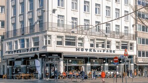 Un hôtel à plusieurs étages, de style architectural classique, doté d’une entrée imposante avec une enseigne, d’un espace extérieur aménagé pour s’asseoir et d’un passage piétonnier.
