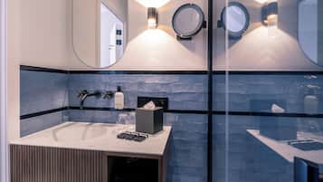 Une salle de bain moderne dotée d’une douche à parois de verre, d’un grand miroir et d’un meuble-lavabo avec un évier et un porte-serviettes.