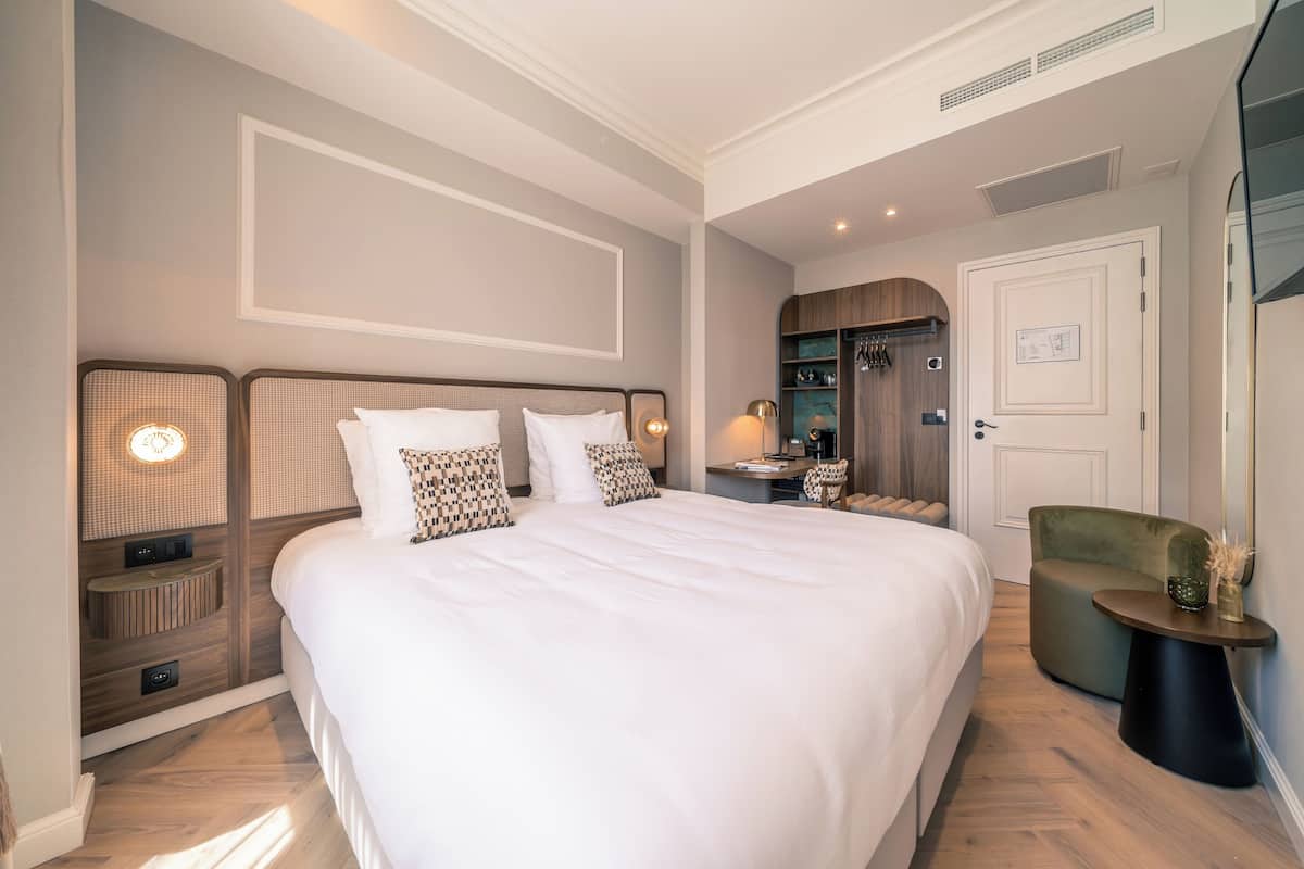 A neatly arranged bedroom with a large bed, bedside tables, a chair, and a mirror.