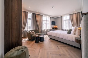 Habitación de hotel moderna con una cama grande, un sofá, dos mesitas de noche y un televisor montado en la pared.