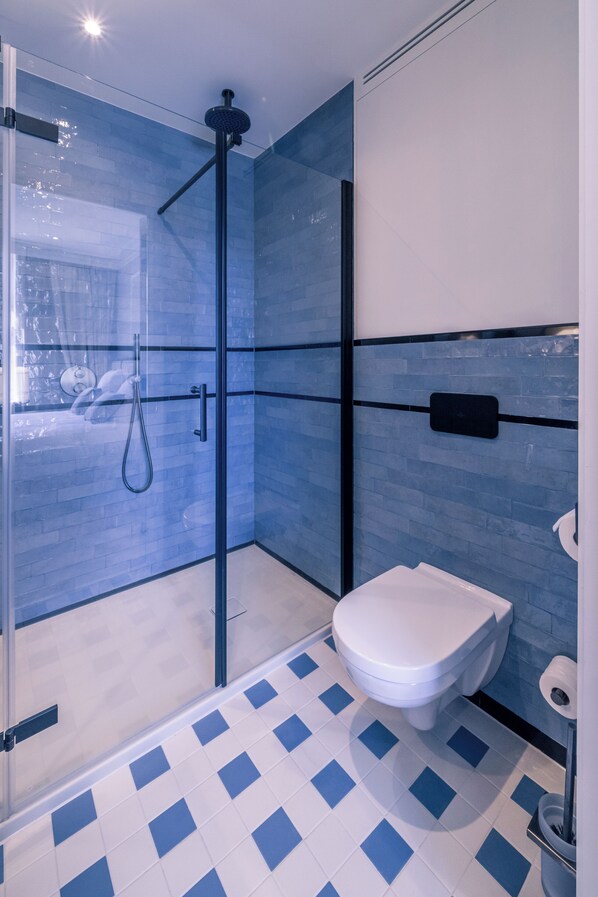 A modern bathroom with a glass-enclosed shower, a white toilet, and a blue-tiled floor. - Hotel Du Parc (Ostend)