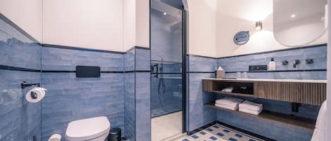 Ein modernes Badezimmer mit einer gläsernen Duschkabine, einer weißen Toilette und einem blau gefliesten Boden.