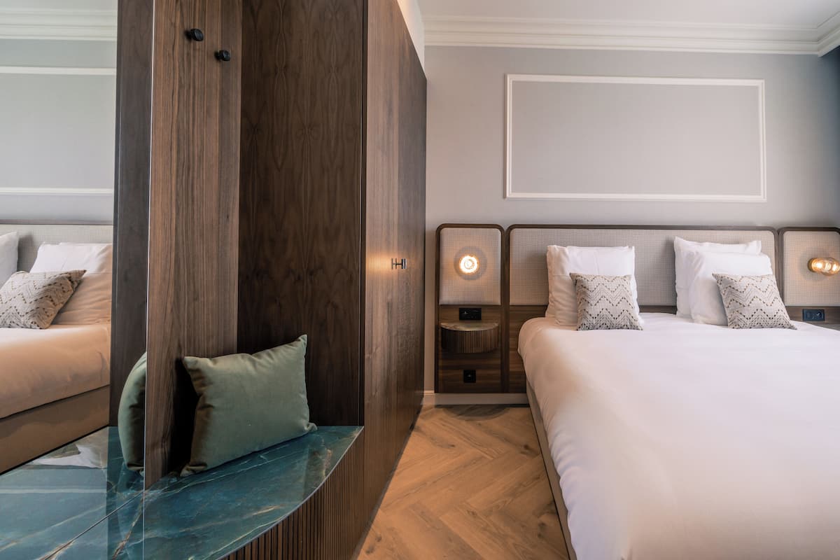A modern hotel room with a large bed, a seating area with a glass table, and a wooden wardrobe.