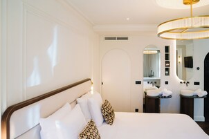 A hotel room with a large bed, two bedside tables, a round mirror, and a modern chandelier.