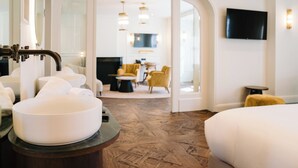 Une chambre d’hôtel avec un grand lavabo rond, un lit, un téléviseur fixé au mur et un coin repas à l’arrière-plan.