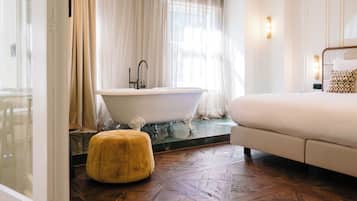 A modern bathroom with a freestanding bathtub, a wooden herringbone floor, and a plush ottoman.