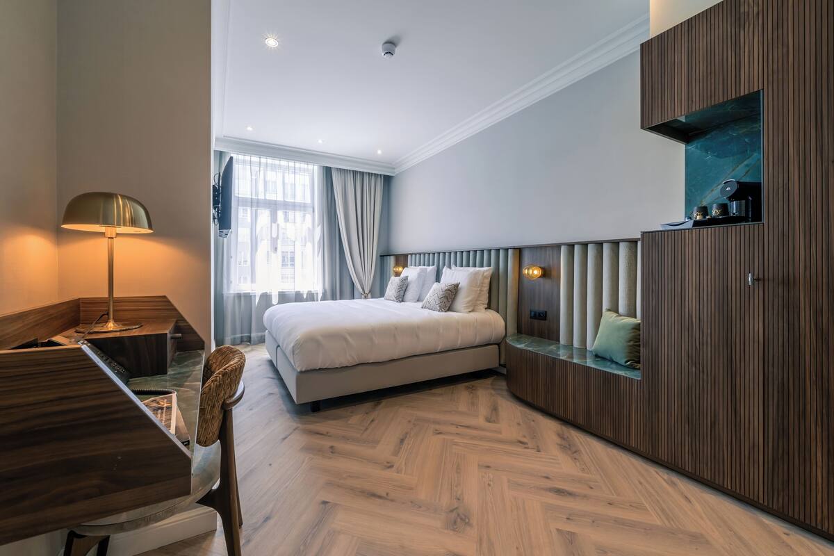 A modern hotel room with a bed, desk, and wardrobe.