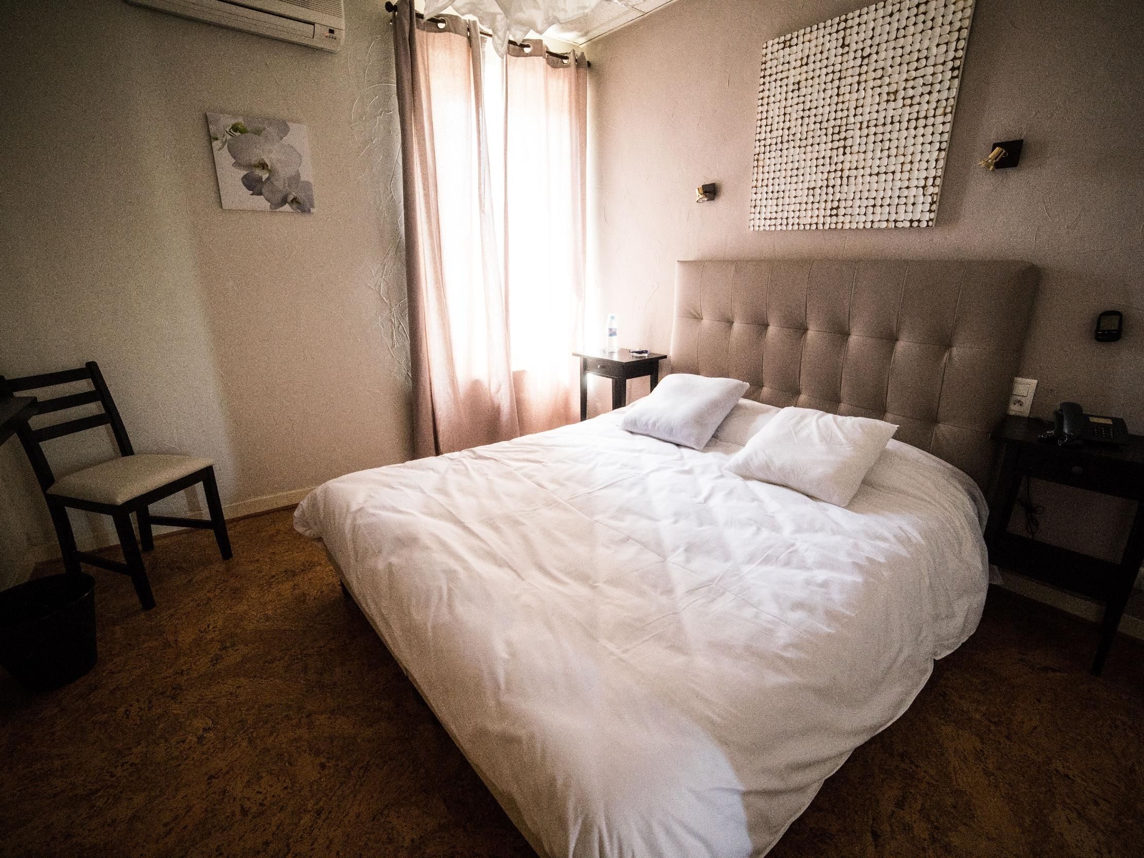A bedroom with a bed, a chair, a bedside table, a wall-mounted light, and a decorative wall piece.