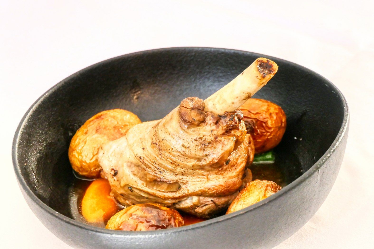 Una ciotola nera con un costolone di agnello arrosto e patate.