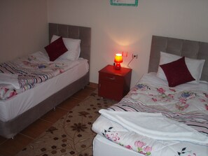 A bedroom with two beds, each with floral bedding and red pillows. There is a nightstand with a lamp between the beds. - Hotel Pamukkale (Denizli)