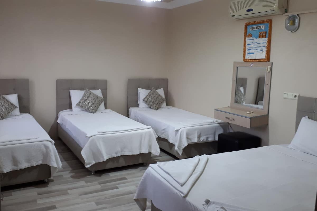 A hotel room with three single beds, a small desk, a mirror, and a wall-mounted air conditioner.