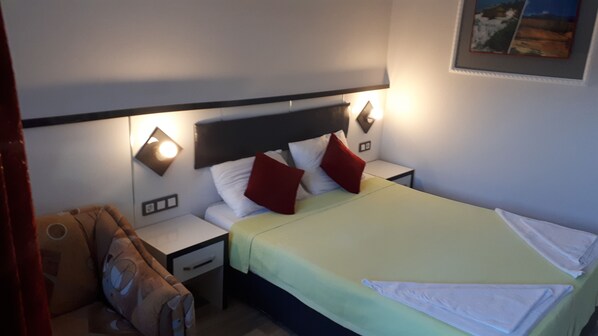 Una habitación de hotel con una cama, mesitas de noche y una lámpara fijada a la pared.