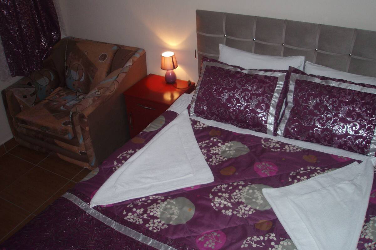 A bedroom with a bed, pillows, a nightstand, and a lamp.
