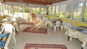 A sunlit dining area with tables and chairs, large windows, and a view of greenery outside. - Hotel Pamukkale (Denizli)