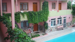 A pink building with a pool, stone walls, and a covered patio area. - Hotel Pamukkale (Denizli)