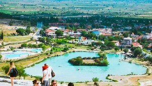 A large outdoor swimming pool with multiple sections and a view of a town in the background. - Hotel Pamukkale (Denizli)