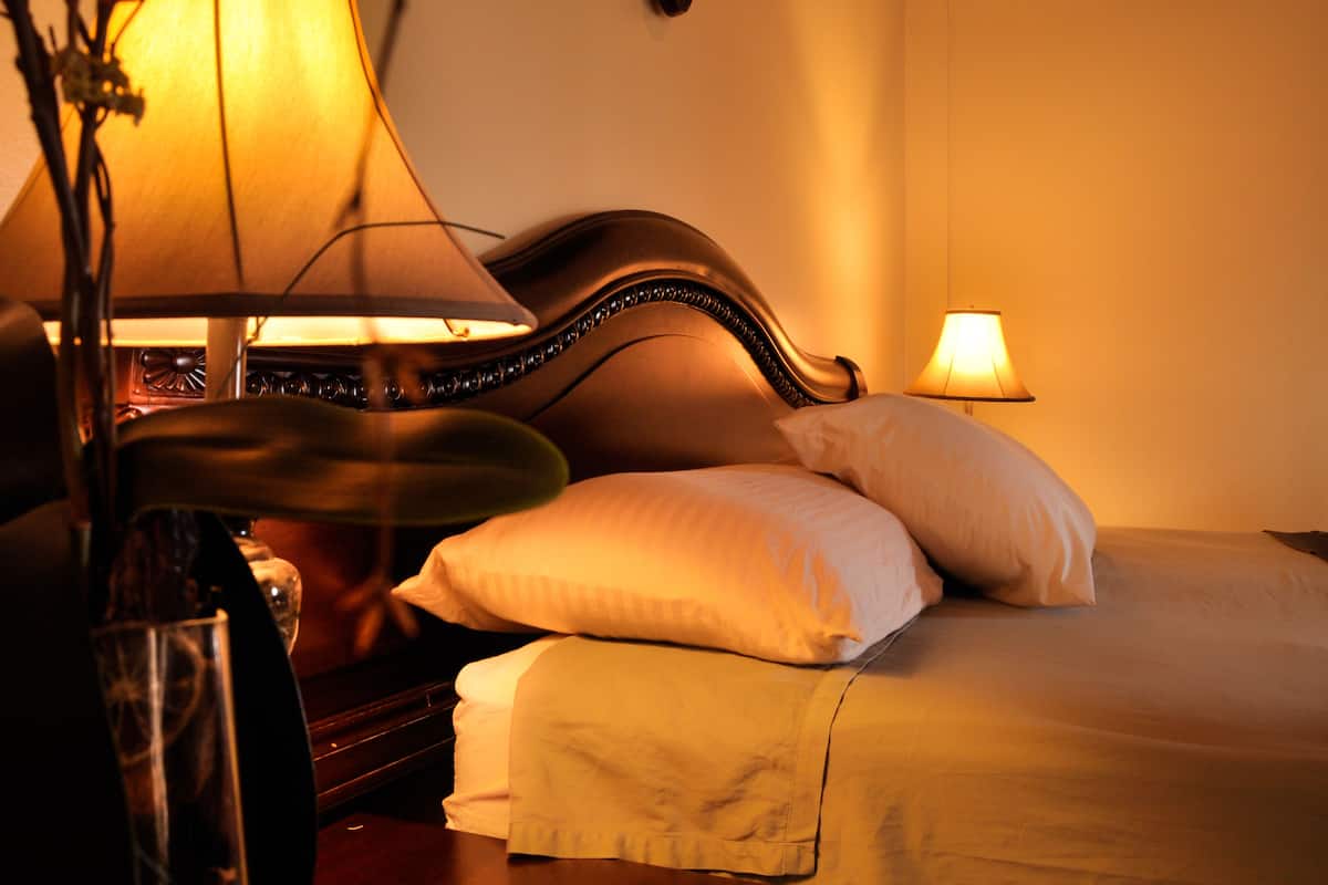 A hotel room with a bed, two bedside lamps, a nightstand, and a glass of water.