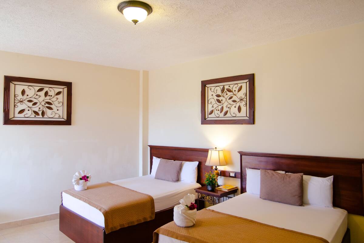 A hotel room with two beds, a ceiling light, and two wall-mounted decorative pieces.
