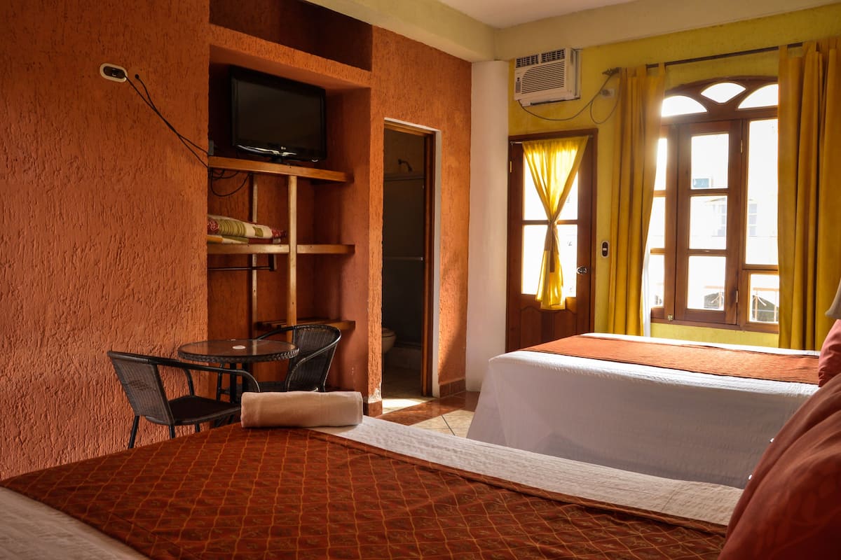 A hotel room with two beds, a television, a small table with chairs, and a window with curtains.