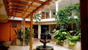 Un patio con una fuente en el centro, rodeado de plantas en macetas y una pérgola de madera.