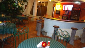 Un restaurante con mesas y sillas redondas, una zona de bar y un ventilador de techo.