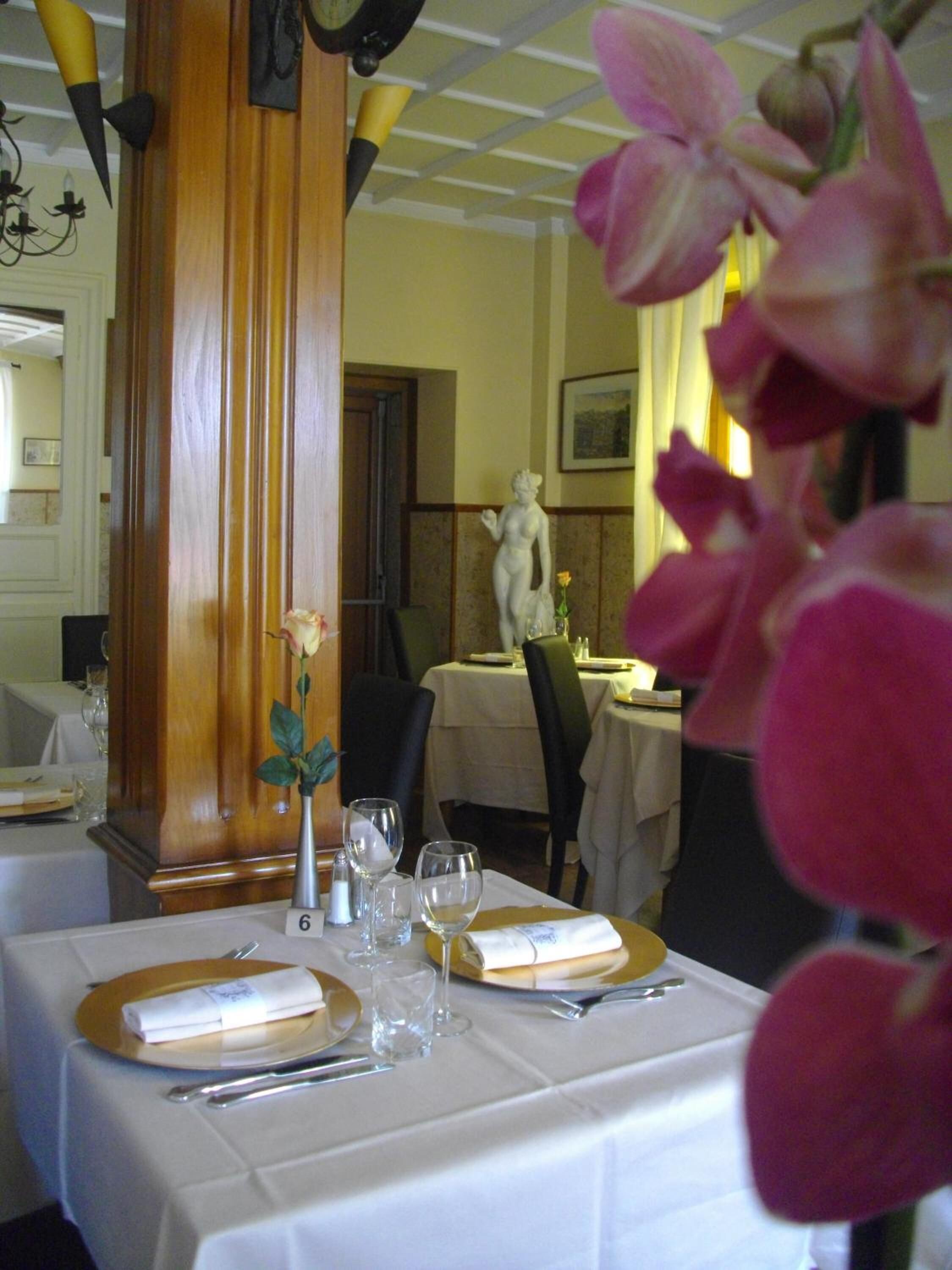 A dining table set with white tablecloths, plates, cutlery, and wine glasses.