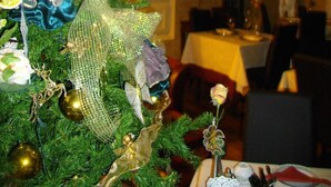 A Christmas tree with ornaments and a decorative angel in a dining area with a chandelier and a table set for a meal.