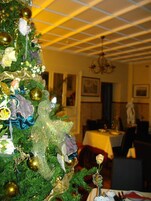 Árvore de Natal com enfeites e um anjo decorativo em sala de jantar com lustre e mesa posta para refeição.