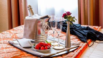 A neatly arranged bed with a champagne bucket, two glasses, a rose, and strawberries.