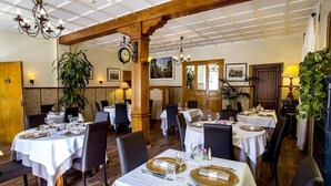 A restaurant with multiple tables set for dining, featuring white tablecloths and gold-rimmed plates.
