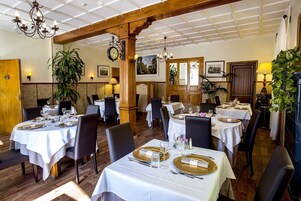 Restaurante com várias mesas preparadas para refeições, com toalhas brancas e pratos com detalhes dourados.