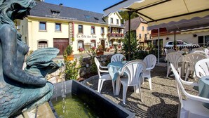 A courtyard with outdoor seating, a fountain, and a building with a sign reading "La Télé des Fous".