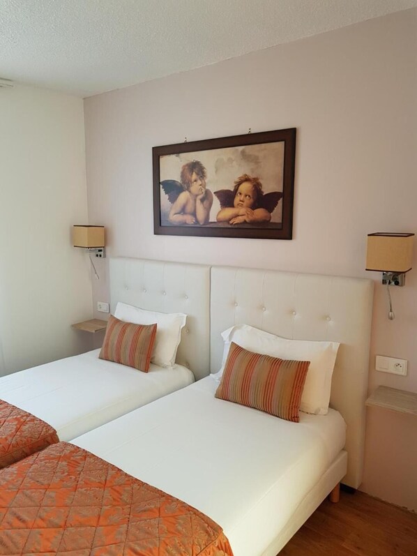 A hotel room with two beds, a painting of cherubs on the wall, and bedside lamps.