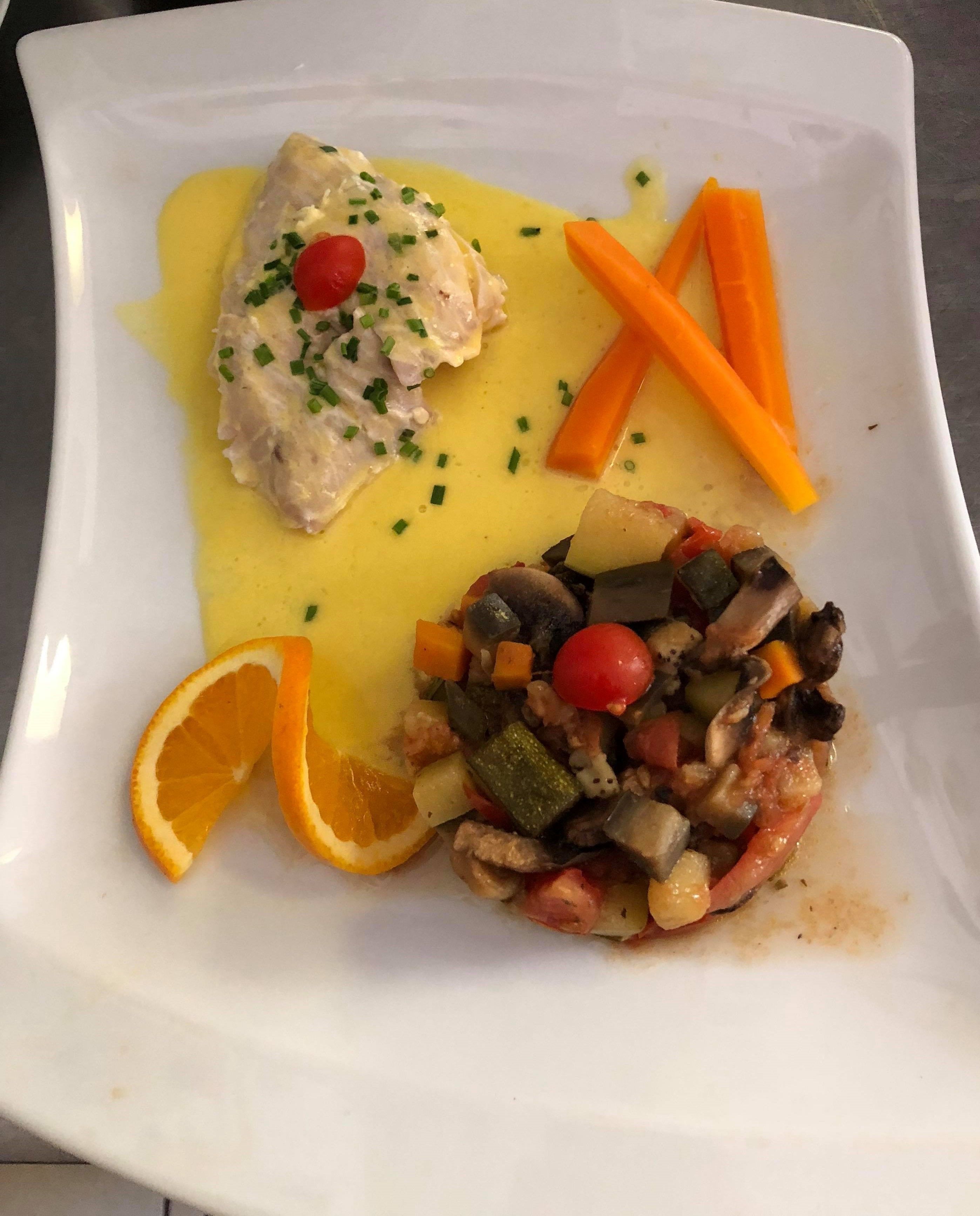 A white plate with a piece of fish, a vegetable medley, and carrot sticks.