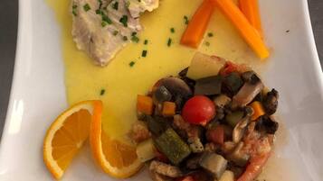 A white plate with a piece of fish, a vegetable medley, and carrot sticks.