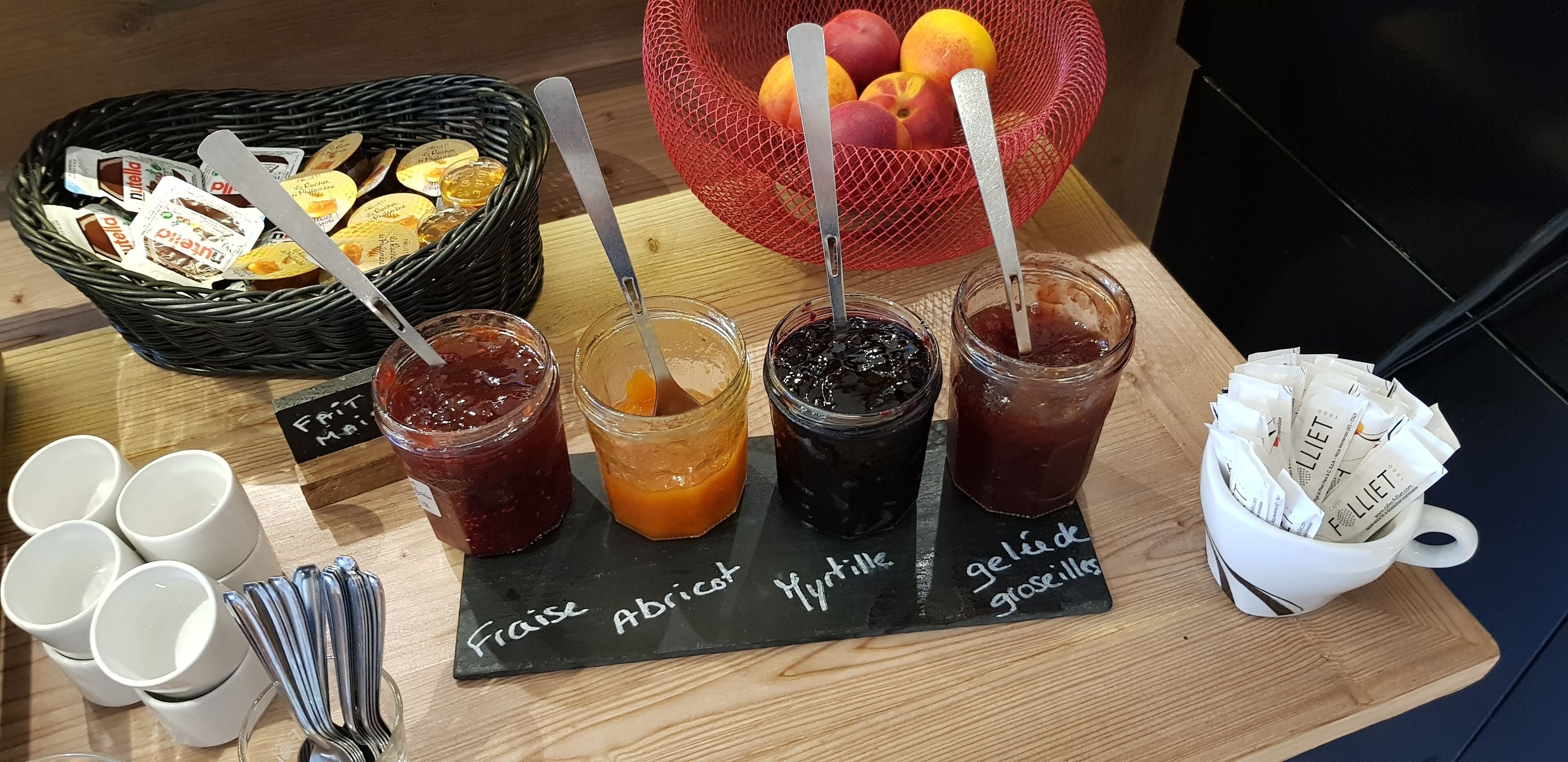 A table with various jams and a basket of fruits.