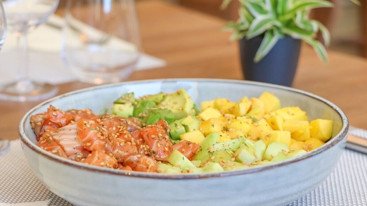 Un tazón de comida con salmón, aguacate y mango.