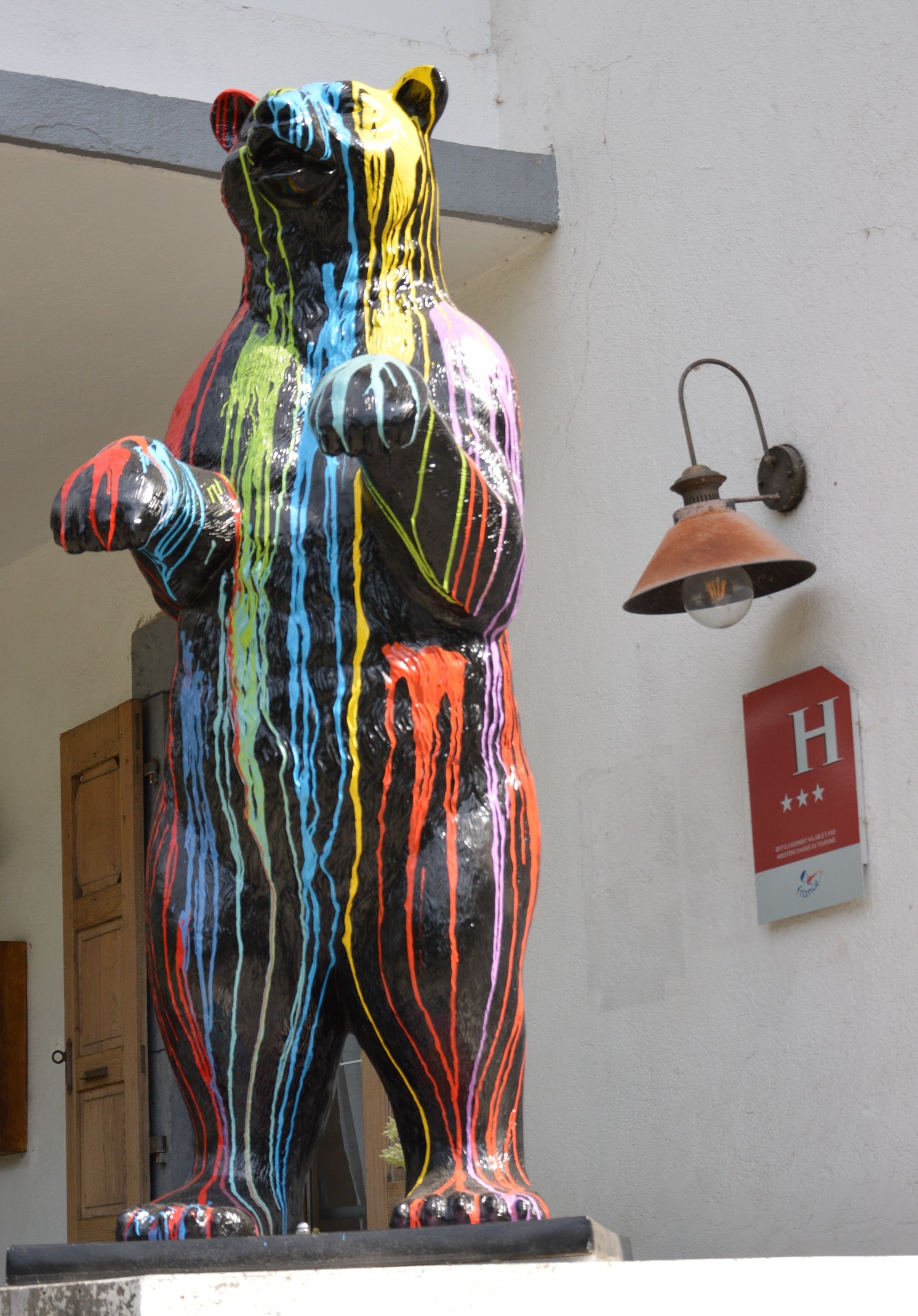 A colorful bear statue with a red sign with an 'H' and three stars on the wall behind it.