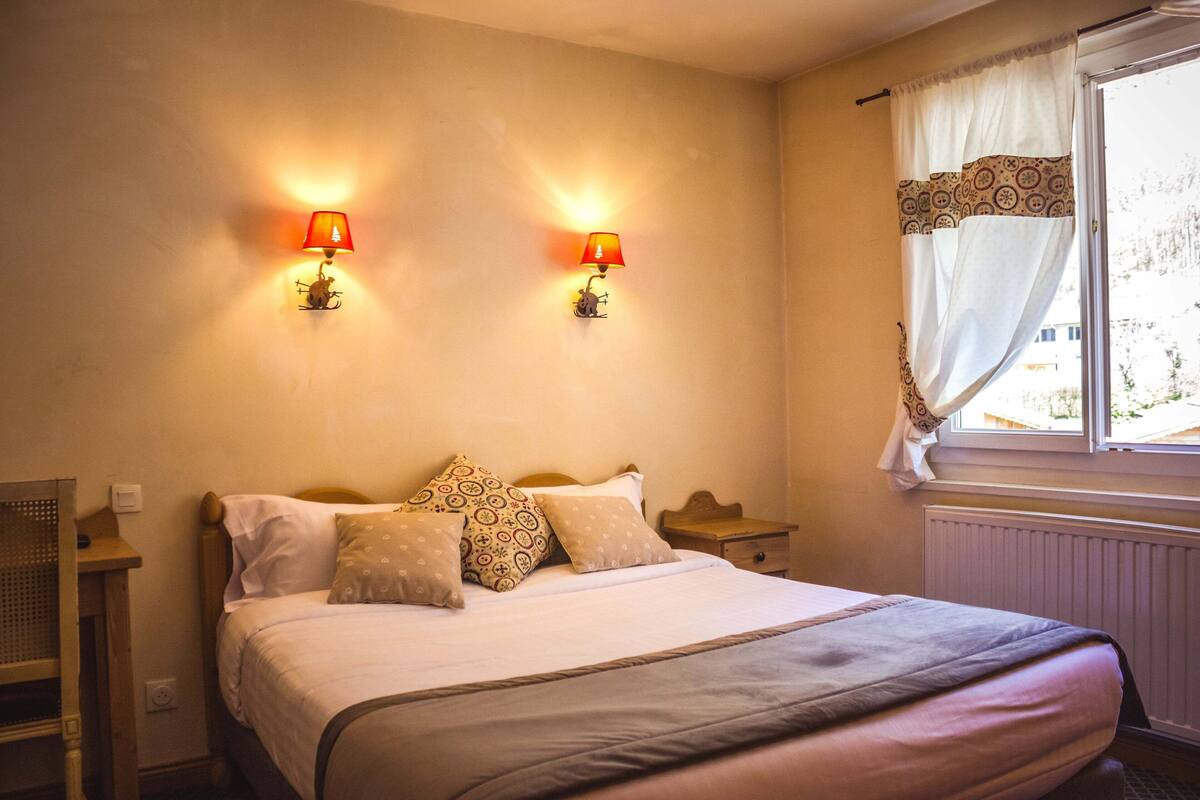 Une chambre à coucher avec un lit, deux lampes fixées au mur, une fenêtre avec des rideaux et une table de chevet.