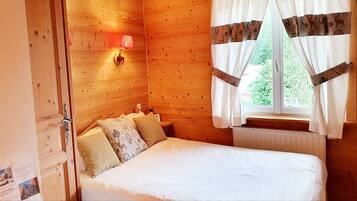 A wooden room with a bed, a wall-mounted lamp, and a window with curtains.